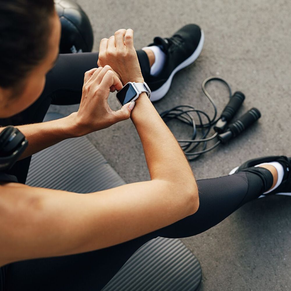 Person sitting on a yoga mat using a smartwatch with jump ropes in the background